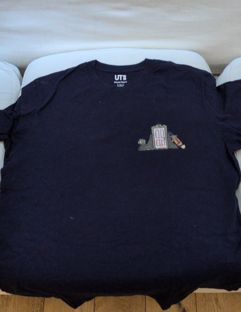 Navy blue short-sleeved t-shirt with a small printed monster-factory door on the chest and, on the reverse, the arched text "SULLEY&MIKE / WE SCARE BECAUSE WE CARE" above cartoon blue and green monsters.