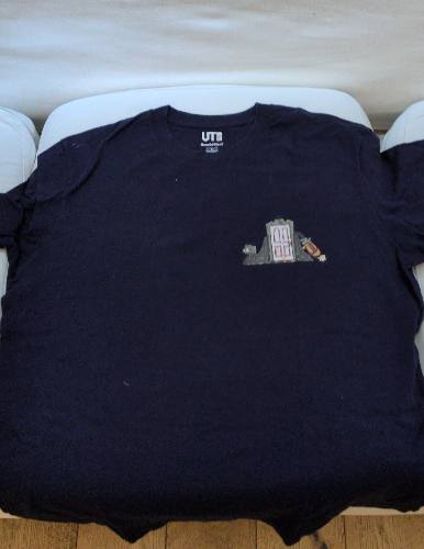 Navy blue short-sleeved t-shirt with a small printed monster-factory door on the chest and, on the reverse, the arched text "SULLEY&MIKE / WE SCARE BECAUSE WE CARE" above cartoon blue and green monsters.